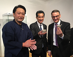 Zu sehen sind Hideki Inoue, Bürgermeister Shinju Yamaguchi und Oberbürgermeister Markus Ibert mit handgefertigten Tongefäßen in den Händen. Hideki Inoue (links) trägt einen dunkelblauen Kimono, Shinju Yamaguchi trägt einen schwarzen Nadelstreifenanzug mit einer blau-weiß gemusterten Krawatte, OB Markus Ibert einen dunkelblauen mit lila Krawatte. Sie stehen im Stadtmuseum vor einer Glasvitrine.