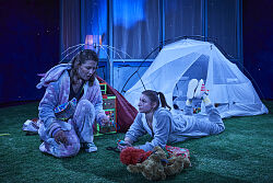 Nächtliche Szene auf der Theaterbühne mit zwei Mädchen vor einem weißen Zelt