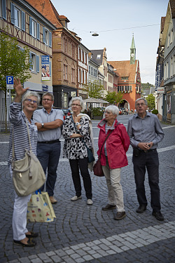 Das Bild zeigt eine Stadtführerin während der Führung mit ihren Gästen in der Kaiserstraße. Im Hintergrund das alte Rathaus.