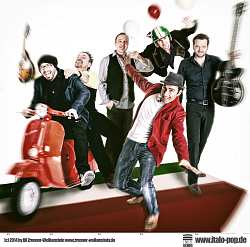 Das Foto zeigt eine Musikgruppe mit sechs Männern. Zwei Männer sitzen auf einem Motorroller. Teilweise haben die anderen Männer Musikinstrumente in der Hand. Ein Mann hat einen Helm auf und fliegt. 