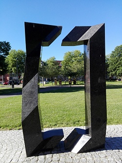 Zu sehen ist ein modernes geometrisches Kunstwerk aus schwarzem Granit von Hiromi Akiyama im Park am Friedrich-Ebert-Platz. Es ist das größte Kunstwerk im Park.