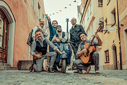 Sechs Männer, einer davon mit Gitarre, mit einem Roller in einer Gasse