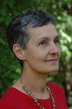 Portraitbild von Ingeborg Gleichauf. Sie trägt kurzes Haar, das teilweise grau ist. Sie hat ein rotes Oberteil an und trägt eine Kette aus silbernen Elementen und beige-braunen Kugeln.