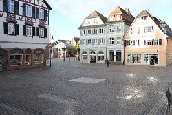Quadratische Steinplatte in einem Platz mit Kopfsteinpflaster, umgeben von Häuserfassaden