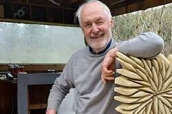 Zu sehen ist ein Mann mit einer kleinen Kettensäge vor einem rechteckigen Holzobjekt