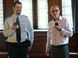 Jochen Brehm von der Polizei in Uniform und Stefan Langenkamp halten ein Funkgerät in Händen. 