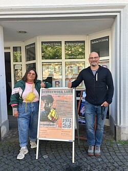 Gamze und Thomas stehen neben einem Plakat, worauf Steetwork Lahr steht vor dem neuen Jugendraum. 