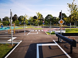 Blick auf den Übungsplatz der Jugendverkehrsschule Lahr. Zu sehen ist eine Kreuzung uns verschiedene Verkehrszeichen, außerdem eine Kreisverkehr und andere Übungselemente für junge Radfahrer. Dazwischen wurde Rasen angelegt, die einzelnen Elemente sind bunt und kindgerecht gestaltet.