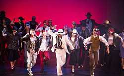 Viele Menschen tanzen eine schwungvolle Choreographie in verschiedensten Outfits. Die meisten tragen Hüte.