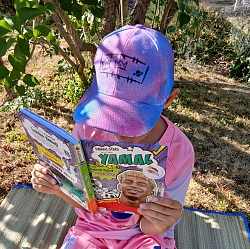 Kind mit bunter Kappe sitzt draußen und liest ein Buch mit dem Titel &#39;YAMAL&#39;