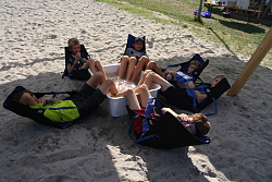 Das Bild zeigt Jungen, die beim Sommerferienprogramm des Kinder- und Jugendbüros im Sand sitzen und die Füße in einer Schüssel mit Wasser entspannen.