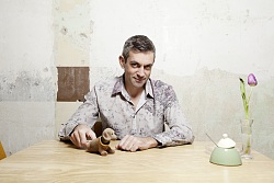 Wladimir Kaminer sitzt an einem Tisch mit Blume, Zuckerdose und Wackeldackel.