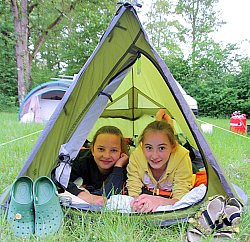 Zwei Mädchen liegen auf dem Bauch in einem kleinen Zelt und schauen vorne heraus.