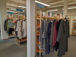 Kleiderstangen sind zwischen Bücherregalen installiert, auf ihnen hängen verschiedene Kleidungsstücke.