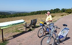 Helmut Schönberger mit dem Pedelec auf dem Langenhard. Er zeigt auf das traumhafte Panorama, das sich von dort bietet.