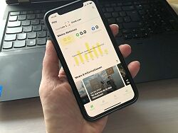 Eine Hand hält ein Smartphone, auf dem die Oberfläche der App 2Zero zu sehen ist. Im Hintergrund ein Laptop.