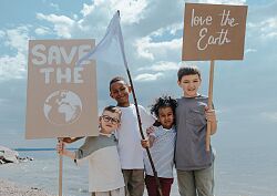 Vier Kinder stehen an einem Strand und halten Schilder, auf denen steht: &#34;Save the world&#34; und &#34;Love the earth&#34;