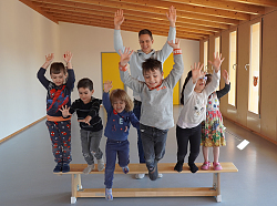 Sechs Kinder stehen auf einer Bank, reißen die Hände nach oben und springen jubelnd runter. Im Hintergrund der FSJler. 