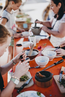 Das Foto zeigt Kinder wie sie an einem Tisch sitzen und mit Hilfe von Mörsern und anderen Hilfsmittteln Kräuter herstellen 