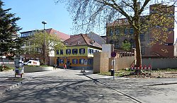 Das Bild zeigt einen Blick in doe Kreustraße vor der Umbaumaßnahme. rechts sieht man das rote Ziegelgebäude der ehemaligen Tonofenfabrik, das gerade zum Stadtmuseum ausgebaut wird. In der Bildmitte ist ein farbenfrohes Haus mit rotem Ziegeldach und einer im ersten Stock orange und im zweiten gelb gestrichenen Fassade zu sehen.