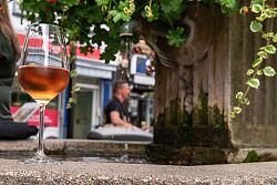 Weinglas mit Roséwein. Im Hintergrund unscharf ein Baum, Hausfassade und ein Mann.