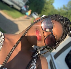 Die Künstlerin lächelt die schräg gehaltene Kamera an. In der Sonnenbrille, die sie trägt, reflektiert die Sonne.