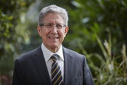 Das Bild zeigt Oberbürgermeister Dr. Wolfgang G. Müller. Er hat graue, kurze Haare, trägt eine eckige, im unteren Bereich rahmenlose Brille, einen blauen Anzug, ein weißes Hemd und eine blaue Krawatte mit gelben, diagonalen Streifen.