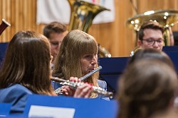Flötenspielerin mit blonden Haaren, herangezoomt, umgeben von unscharfen Musikern in mittelblauer Uniformjacke 