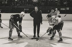 Schwarz-Weiß-Aufnahme von Eishockeyspielern auf der Eisfläche am Anspiel mit Schiedsrichtern