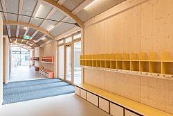 Innenraum mit heller Holzverkleidung und Kindermöbeln und Spielgeräten. Im Hintergrund Fensterfront.