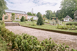 Das Foto zeigt im Hintergrund die Orangerie des Lahrer Stadtparks und den Rosengarten mit den grünen Hecken, Büschen und Bäumen.