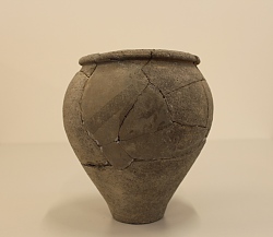 es ist ein grauer Topf zu sehen, der aus Scherben wieder zusammengesetzt wurde.