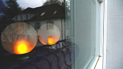 Zwei beleuchtete Kugeln leuchten hinter einem Fenster des Rathauses mit gelben Licht. In den Fenstern spiegelt sich der Südflügel des Rathauses. 