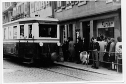 Das Foto zeigt im Vordergrund das Bähnle an einer Haltestelle. Daneben eine Schlange von Menschen, die einsteigen wollen. 