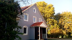 Die Sporthalle der Gesang- und Sportvereinigung Mietersheim e.V. ein graues Gebäude mit Spitzgiebel, weiß umrandeten Fenstern und einem roten Ziegeldach. Der Eingang ist mit einem ebenfalls aus roten Ziegeln bestehenden Vordach versehen. Rings um die Halle herum stehen Laubbäume und Büsche.