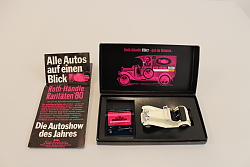 Zu sehen ist eine rechteckig Schachtel in schwarz. Sie ist aufgeklappt. Darin findet sich ein weißer Miniatur-Oldtimer sowie ein Zündholzbriefchen von Roth-Händle. Die Umrisse des Oldtimers sind im Inneren des Deckels pinkfarben abgebildet. Neben der Schachtel liegt ein zusammengefaltetes Werbeprospekt von Roth-Händle zu Oldtimern.