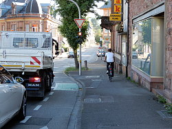 Radfahrer umfährt auf dem Gehweg eine rote Ampel. Auf der Straße steht ein LKW und ein Auto an der roten Ampel.
