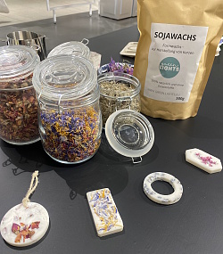 Das Foto zeigt Blüten und Kräuter in Gläsern und Sojawachs 