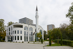 Weiße Moschee mit Minarett, im Hintergrund zwei Hochhäuser
