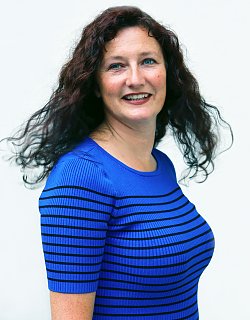 Foto von Florence Millon. Sie hat langes dunkelbraunes, lockiges Haar und trägt einen blauen Pullover mit kurzen Ärmeln und dünnen, schwarzen Querstreifen. Sie lacht und ihre blauen Augen strahlen.