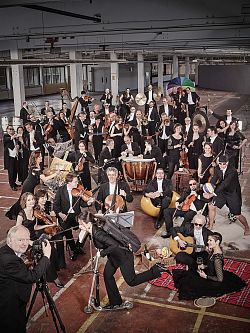 Männer und Frauen des gesamten Orchesters in eleganter schwarzer Kleidung in legeren Posen, beispielsweise beim Wein trinken, Volleyball spielen, zusammensitzen, mit buntem Regenschirm und so weiter.