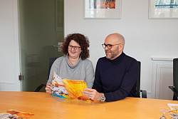 Das Foto zeigt eine Frau und einen Mann, die gemeinsam das neue Programmheft der Volkshochschule anschauen. Die beiden sind sehr fröhlich. 