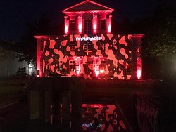 Das Rathaus 1 in Lahr, am Abend, mit roten Scheinwerfern angestrahlt. An der Fassade ist ein camouflageartiges Muster erkennbar und der Hashtag #nightoflight2020.