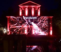 Das Rathaus 1 in Lahr, am Abend, mit roten Scheinwerfern angestrahlt. An der Fassade ist ein Muster erkennbar, das aussieht wie ein Blitz oder ein Wurzelgeflecht, außerdem der Hashtag #nightoflight2020.