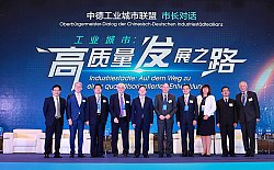 Auf dem Bild ist Oberbürgermeister Dr. Wolfgang G. Müller als zweiter von links in einer Gruppe mit chinesischen und deutschen Arbeitskollegen auf einer Bühne zu sehen. Im Hintergrund sieht man an einer großen Wand nebenchinesischer Schrift auch in deutscher Schrift: Oberbürgermeister-Dialog der Chinesisch-Deutschen Industriestädteallianz 