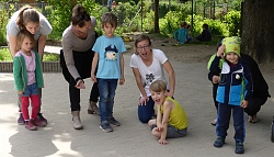 Vier Kinder stehen im Hof nebeneinander und lachen, daneben ihre Mamas, die mit ihnen sprechen.