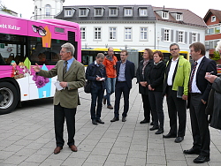 Das Bild zeigt Oberbürgermeister Dr. Müller mit Vertretern der Stadtverwaltung, der SWEG und LGS GmbH sowie Medienvertretern auf dem Rathausplatz vor dem neu gestalteten Bus. Dr. Müller spricht gerade und zeigt auf den Bus, um den Journalisten etwas zu erläutern.