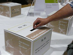 Eine Person steckt ihren Stadtgulden in eine Abstimmungsurne