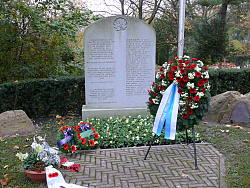 Das Bild zeigt einen Grabstein und einen Kranz mit roten und weißen Blumen davor