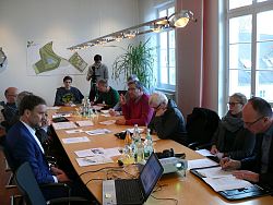 Auf dem Bild ist das Sitzungszimmer im Rathaus 1 in Lahr zu sehen. An einem großen Holztisch sitzen Medienvertreter, Oberbürgermeister Dr. Müller, Markus Ibert und Arnfried Sickinger. Im Hintergrund steht ein junger Mann an einer Kamera und filmt.